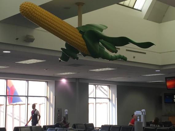 Corn and airplane sculpture hanging from boarding area ceiling