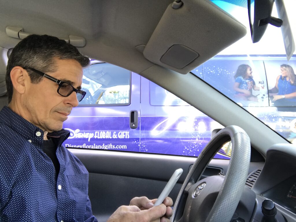 man sitting in parked car looking at phone