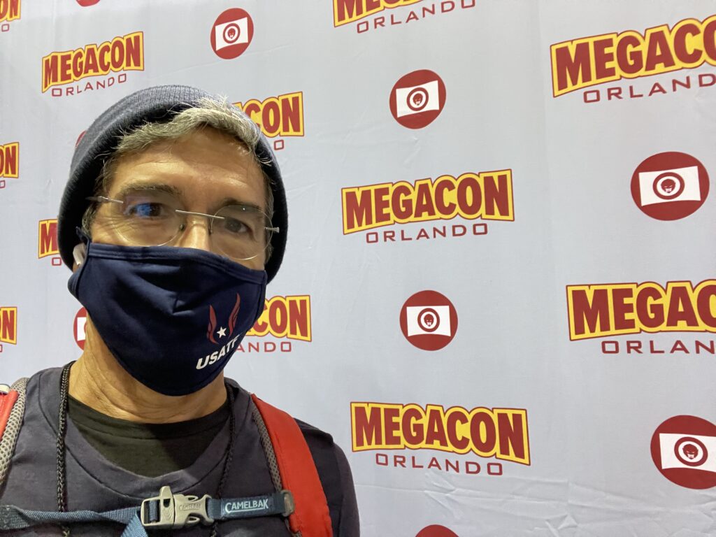 masked man at Mega Con sign