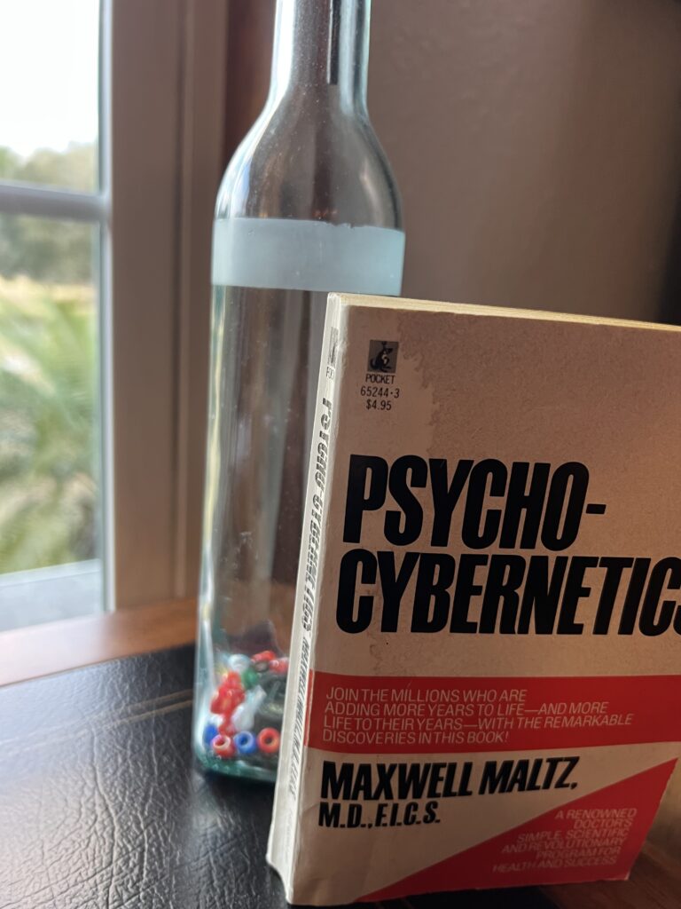 
The book psycho cybernetics and the glass bottle on a desk