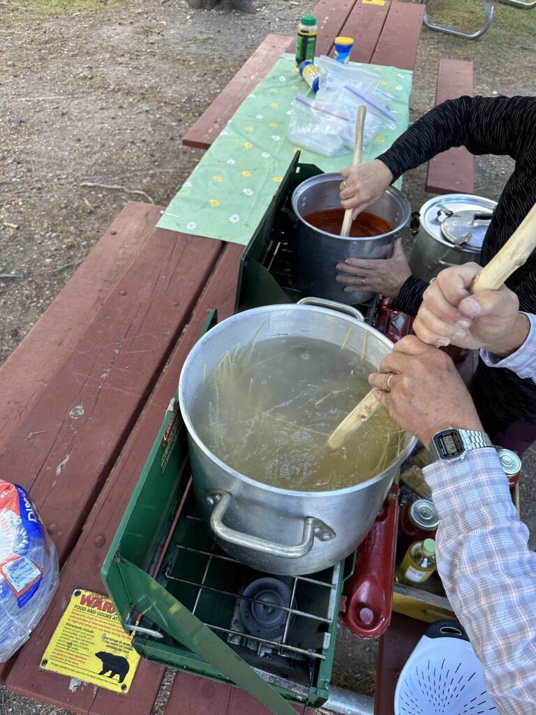 Two people stirring pots on a picnic table